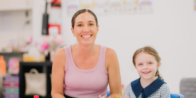 Adult and student seated together at a table in a classroom.